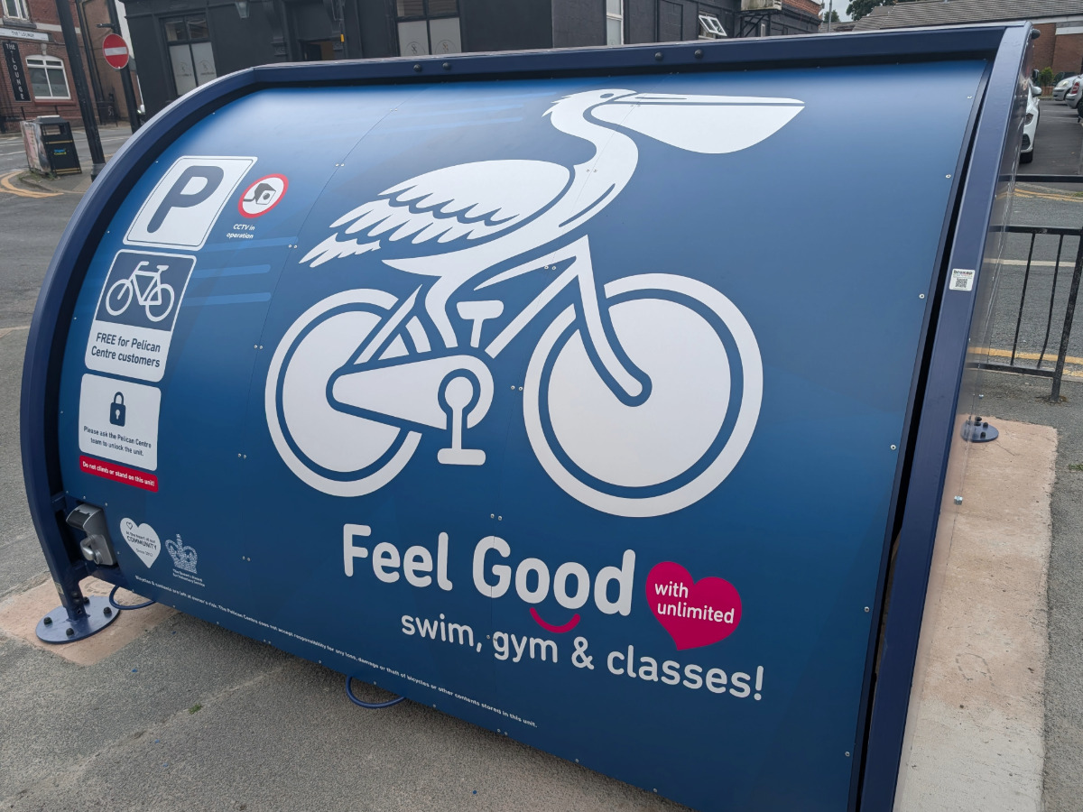 Blue bike storage unit with the design of a pelican riding a bike on the front, placed in the street in front of the Pelican Centre.